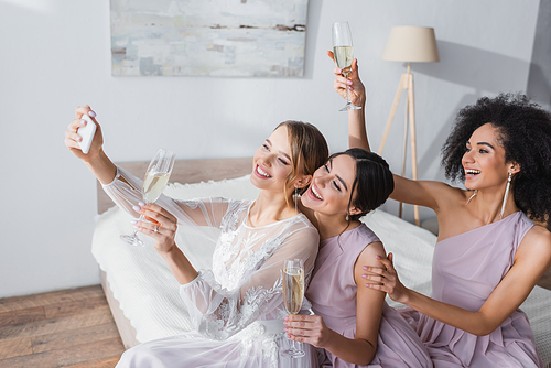 excited bride taking selfie with interracial friends in bedroom