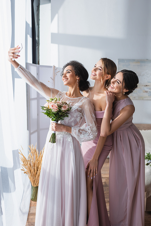 elegant african american bride taking selfie with pretty friends in bedroom