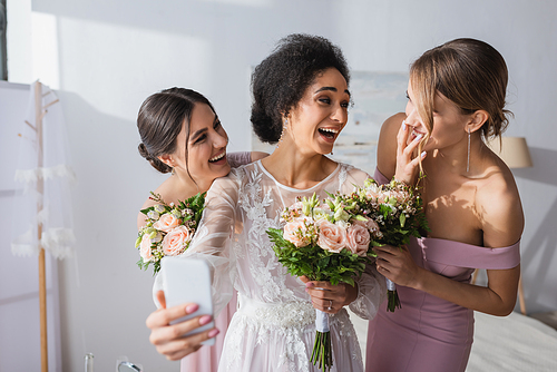 laughing african american bride taking selfie with cheerful friends, blurred foreground