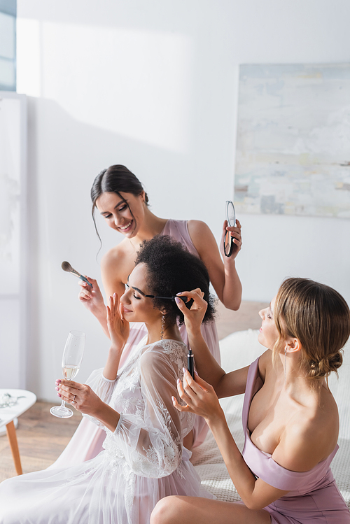 cheerful bridesmaids doing visage to african american bride holding champagne glass