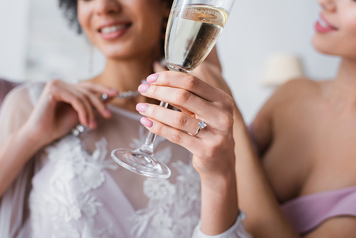 cropped view of african american bride holding champagne glass near bridesmaid on blurred background