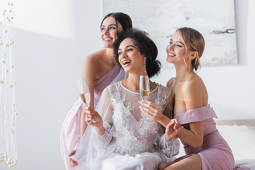 excited african american bride holding champagne near happy bridesmaids