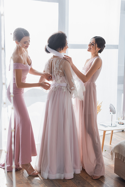 full length view of multicultural bridesmaids preparing african american woman for wedding