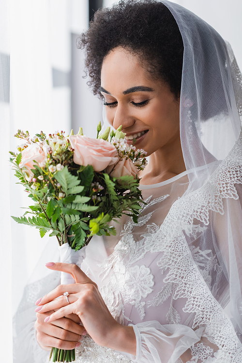 smiling african american bride enjoying smell of wedding bouquet