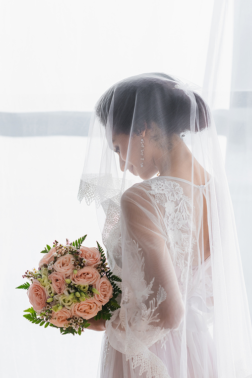 african american bride in veil holding wedding bouquet at home