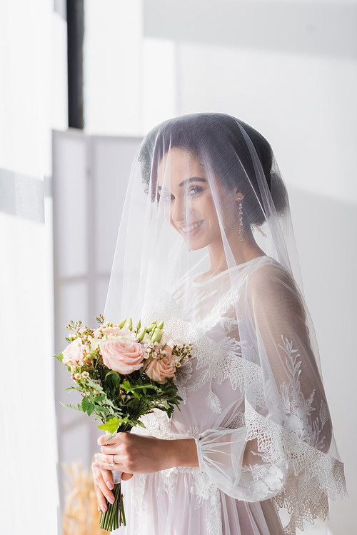 happy african american bride in veil  while holding wedding bouquet