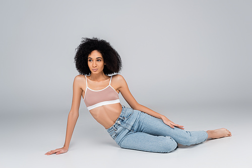 young african american woman with perfect body sitting on grey in jeans and bra