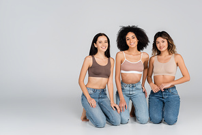 happy interracial women in bras and jeans  on grey