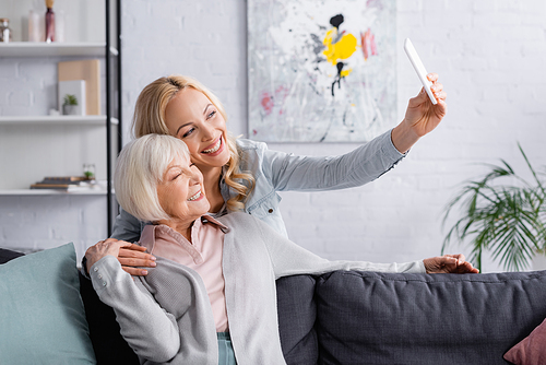 Smiling woman taking selfie with senior parent at home