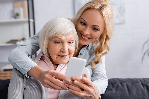 Smartphone on blurred foreground in hands of woman near mother