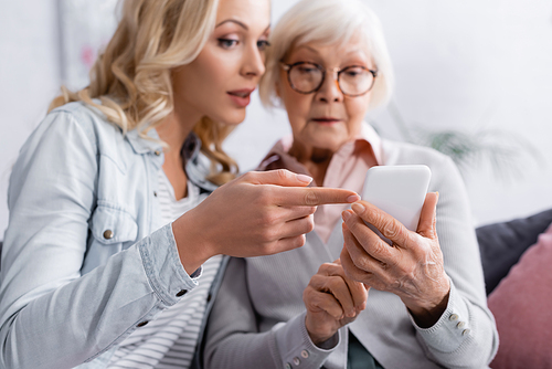 Woman on blurred background pointing with finger at smartphone in hands of senior mother