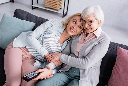 Smiling senior woman watching movie near daughter with remote controller