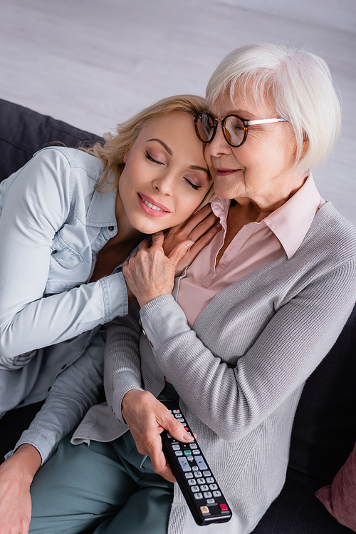 Woman sitting near senior mother with remote controller