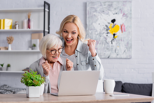 Cheerful mother and daughter showing yes gesture near laptop and cups