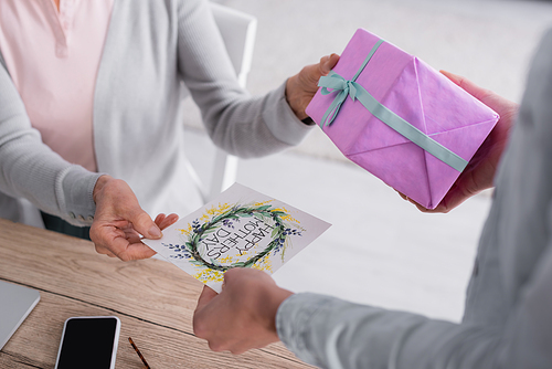 Cropped view of woman giving greeting card and present near senior mother