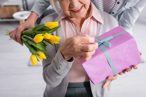 Cropped view of woman holding flowers near elderly mother with present