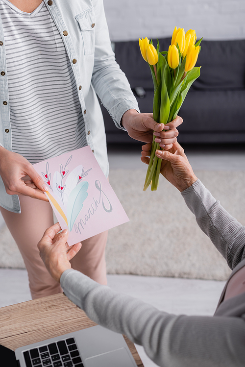 Cropped view of woman giving greeting card with 8 march lettering and flowers to parent at home