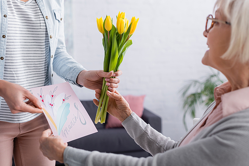 Woman giving greeting card with 8 march lettering and flowers to mother on blurred foreground