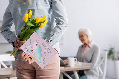 Woman hiding flowers and greeting card with 8 march lettering near mother on blurred background