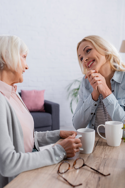 Positive woman talking to mother with cup of tea near eyeglasses