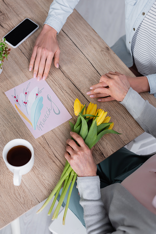 Top view of woman sitting near smartphone, greeting card and senior mother with tulips