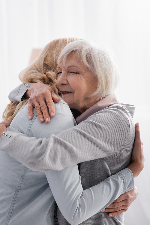 Woman hugging grey haired mom at home