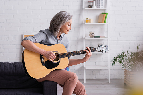mature woman with grey hair playing acoustic guitar in living room