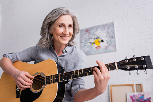 smiling middle aged woman playing acoustic guitar in living room