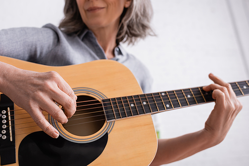 cropped view of middle aged woman playing acoustic guitar in living room