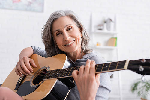 smiling mature woman with grey hair playing acoustic guitar at home