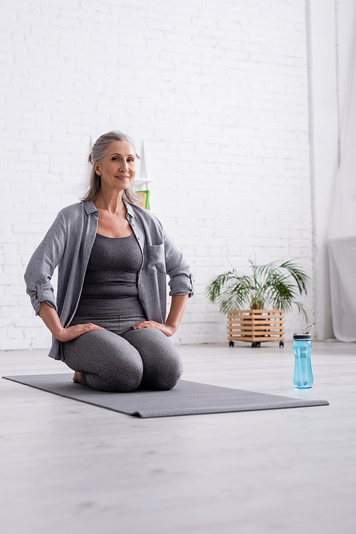 happy mature woman with grey hair practicing yoga near sports bottle