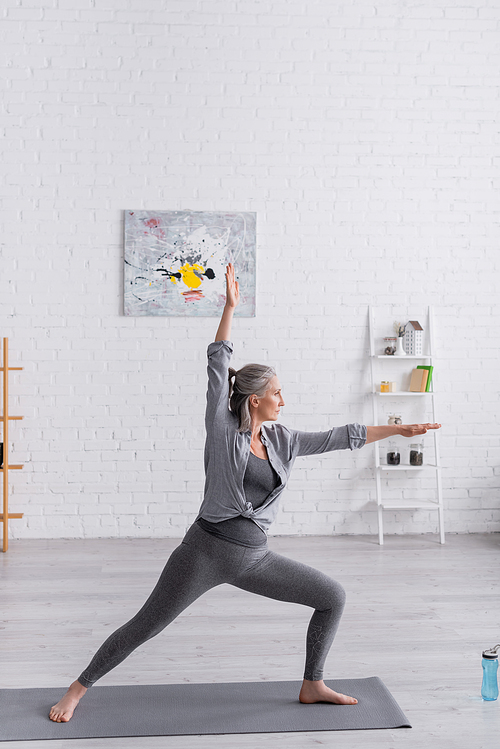 middle aged woman in sportwear standing in warrior pose while practicing yoga