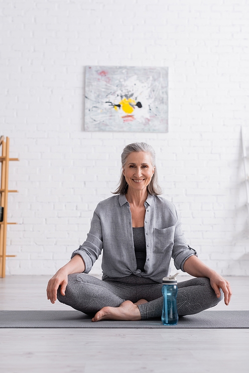 happy middle aged woman sitting in lotus pose on yoga mat