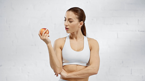 Woman in white sports top looking at red apple