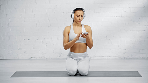 Sportswoman in headphones using smartphone on fitness mat