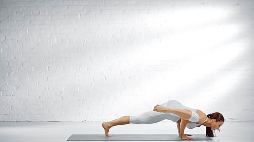 Young woman practicing yoga near white wall at home