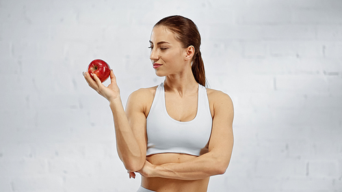 Sportswoman in white sports top looking at ripe apple