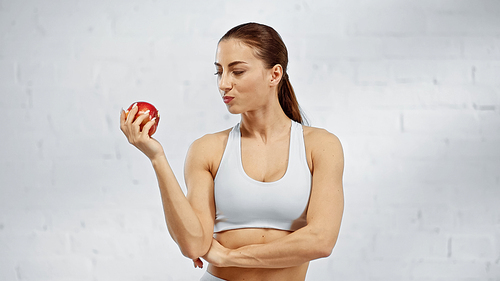 Fit sportswoman looking at fresh apple at home