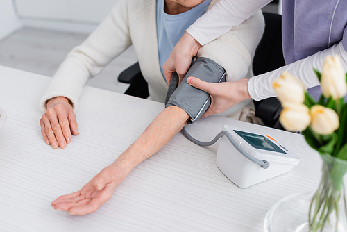 partial view of senior woman and nurse measuring blood pressure with tonometer, blurred foreground