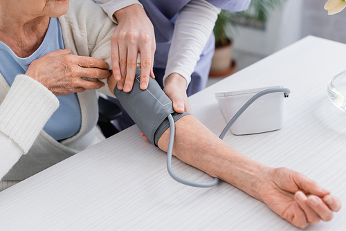 cropped view of social worker measuring blood pressure of senior woman with tonometer