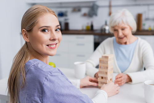happy nurse  while playing wooden tower game with blurred senior woman