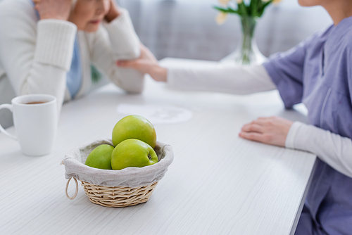 selective focus of fresh apples near nurse calming senior woman sick on dementia, cropped view