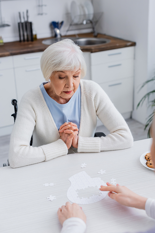 social worker pointing at jigsaw puzzle near senior woman at home