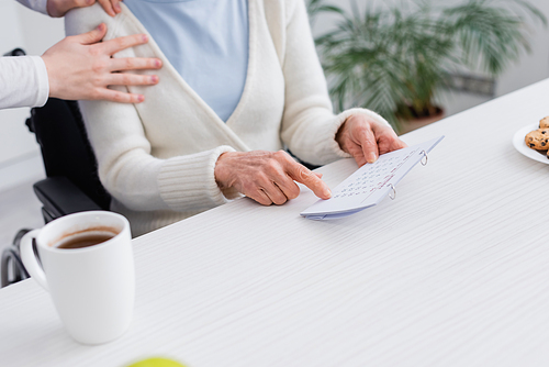 cropped view of nurse touching shoulder of senior woman pointing at calendar while suffering from memory loss