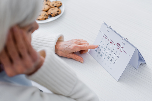 cropped view of elderly woman, suffering from memory loss, pointing at calendar, blurred foreground