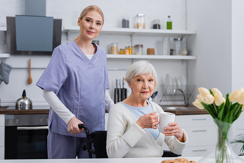 young nurse  near . senior woman with cup of tea in kitchen