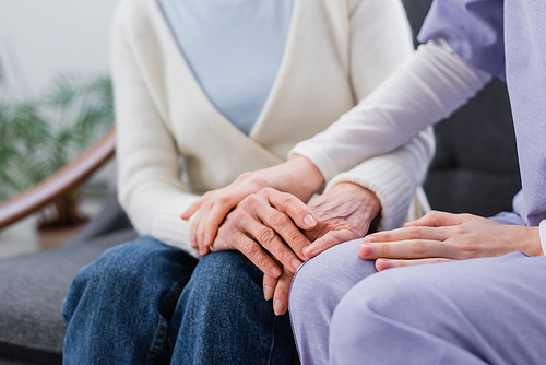 cropped view of nurse touching hand of elderly woman at home