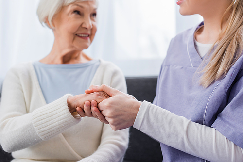 nurse holding hand of aged woman smiling on blurred background