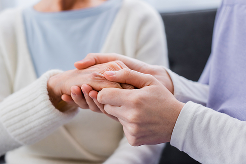 partial view of nurse holding hand of elderly woman, blurred background