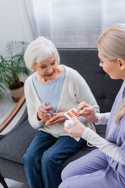 nurse giving medication to senior woman sitting on couch with glass of water